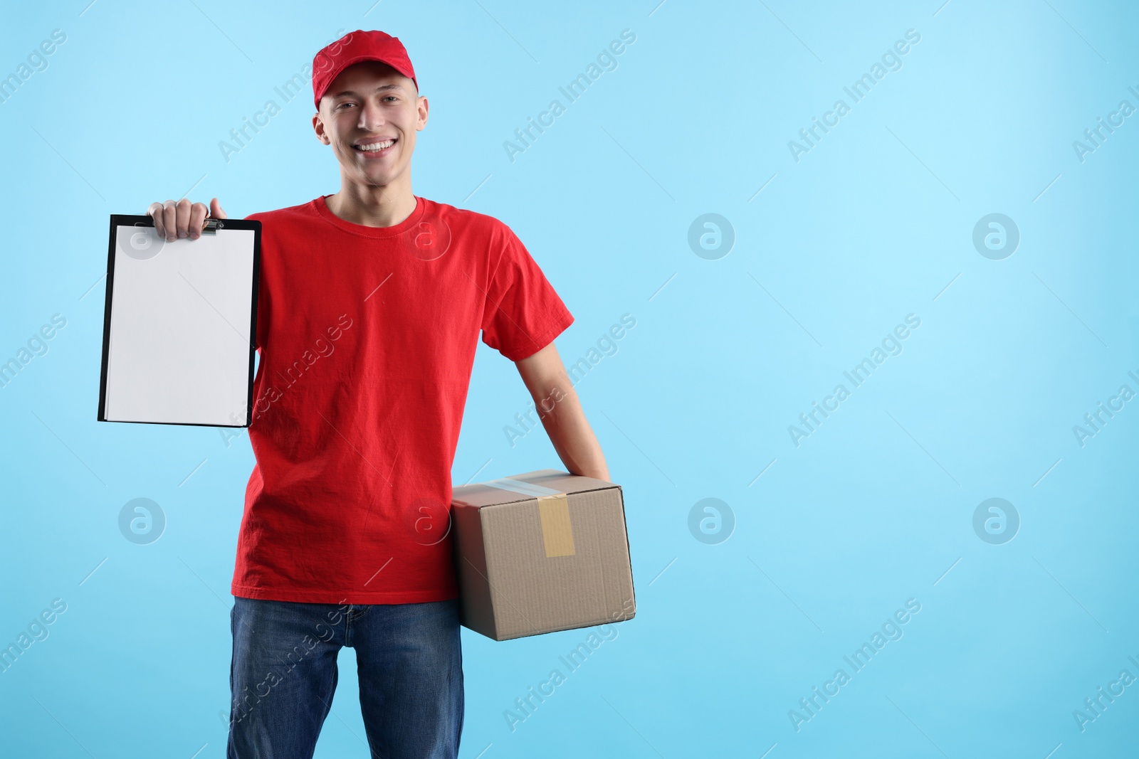 Photo of Happy courier with parcel and clipboard on light blue background. Space for text