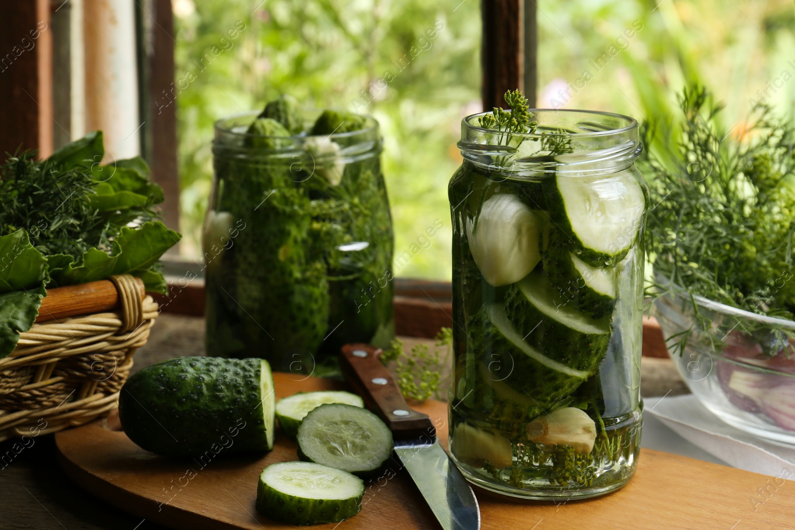 Photo of Glass jars, fresh cucumbers and herbs on wooden table indoors. Pickling recipe