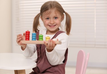 Photo of Cute little girl playing with stacking and counting game at white table indoors. Child's toy