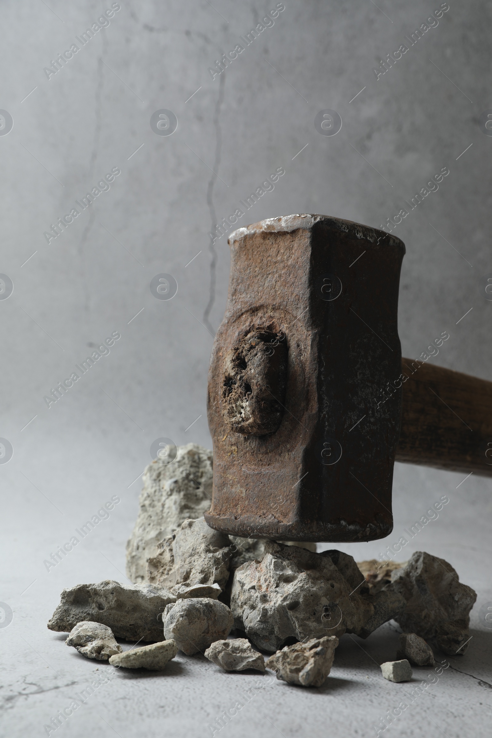 Photo of One sledgehammer and pieces of broken stones on grey background, closeup