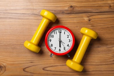 Photo of Alarm clock and dumbbells on wooden table, flat lay. Morning exercise