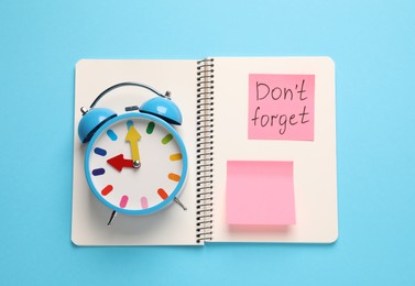 Photo of Alarm clock, notebook and reminder note with phrase Don't forget on light blue background, top view