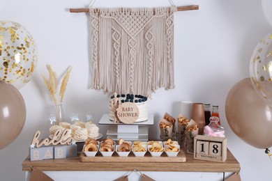 Baby shower party. Different delicious treats on wooden table and decor near light wall