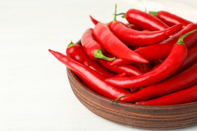 Wooden bowl with red hot chili peppers on white table, closeup. Space for text