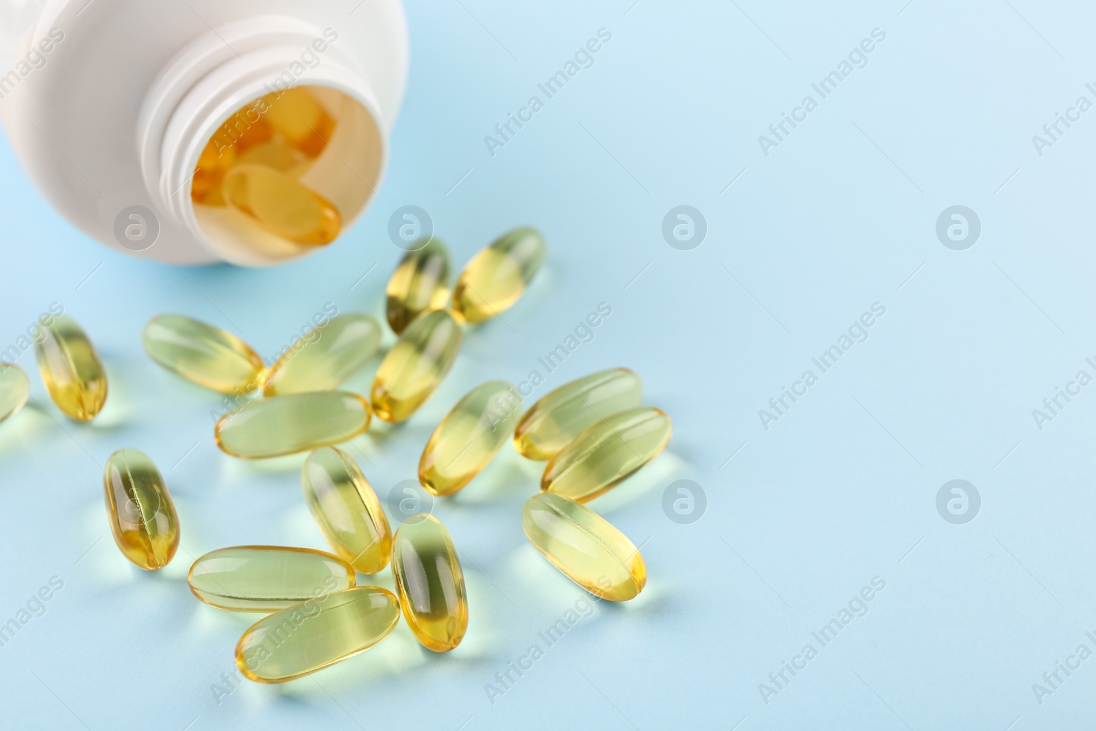 Photo of Bottle and vitamin capsules on light blue background, closeup. Space for text