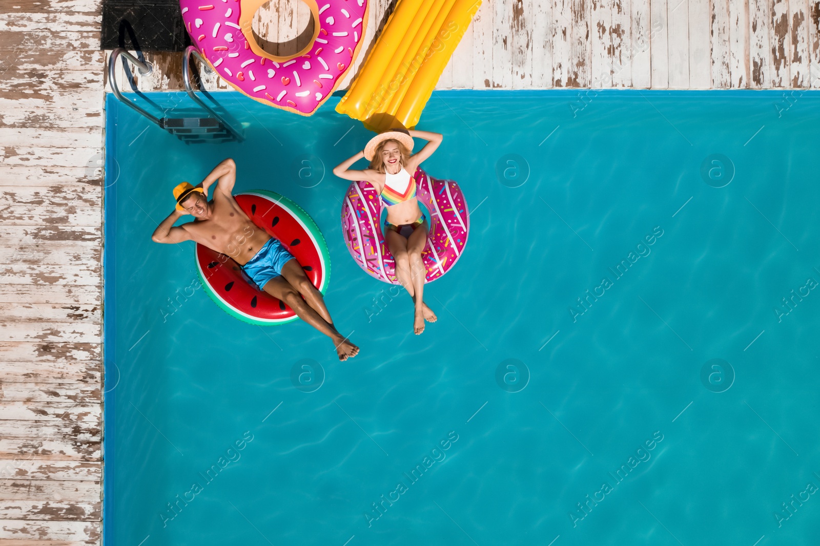 Image of Happy couple with inflatable rings in swimming pool, top view. Summer vacation