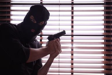 Photo of Man in mask holding gun near window indoors. Space for text