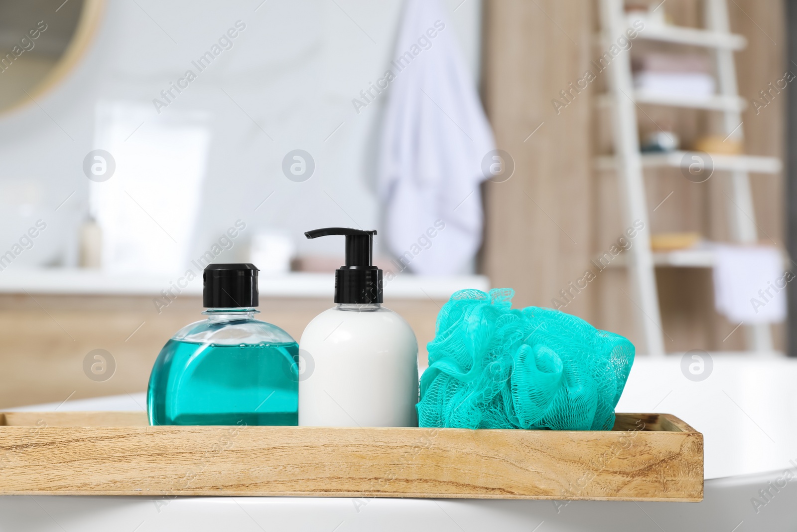 Photo of Wooden bath tray with bottles of shower gels and mesh pouf on tub indoors