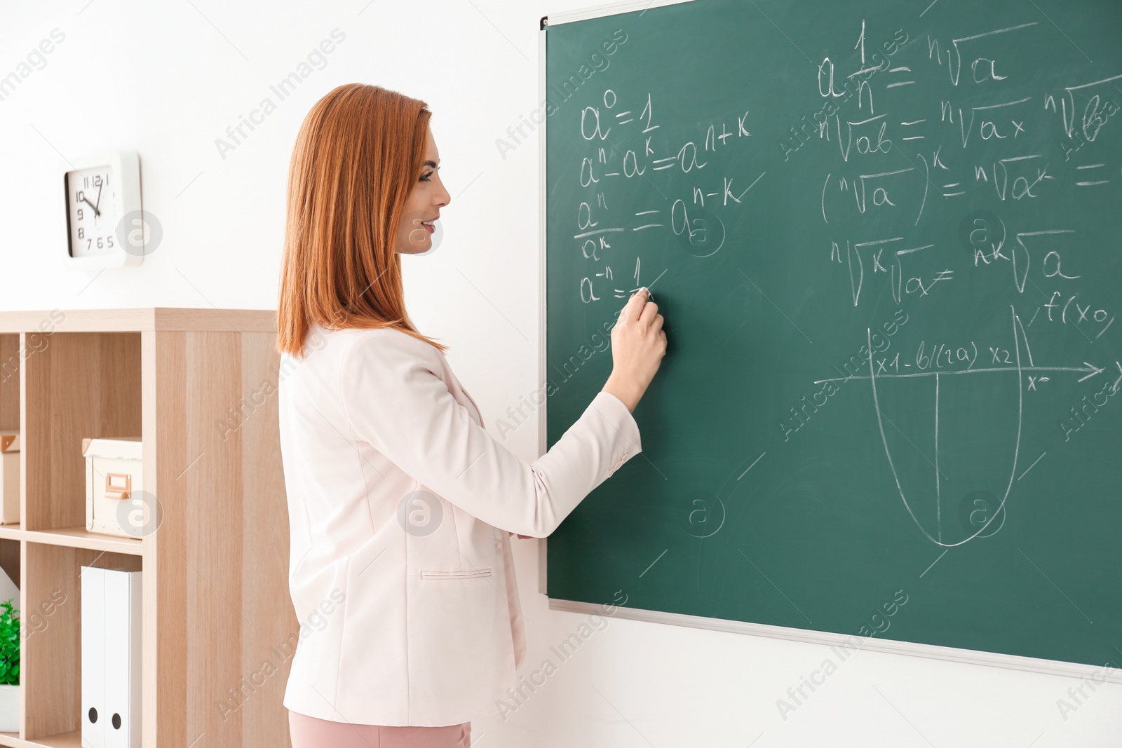 Photo of Beautiful young teacher writing on blackboard in classroom