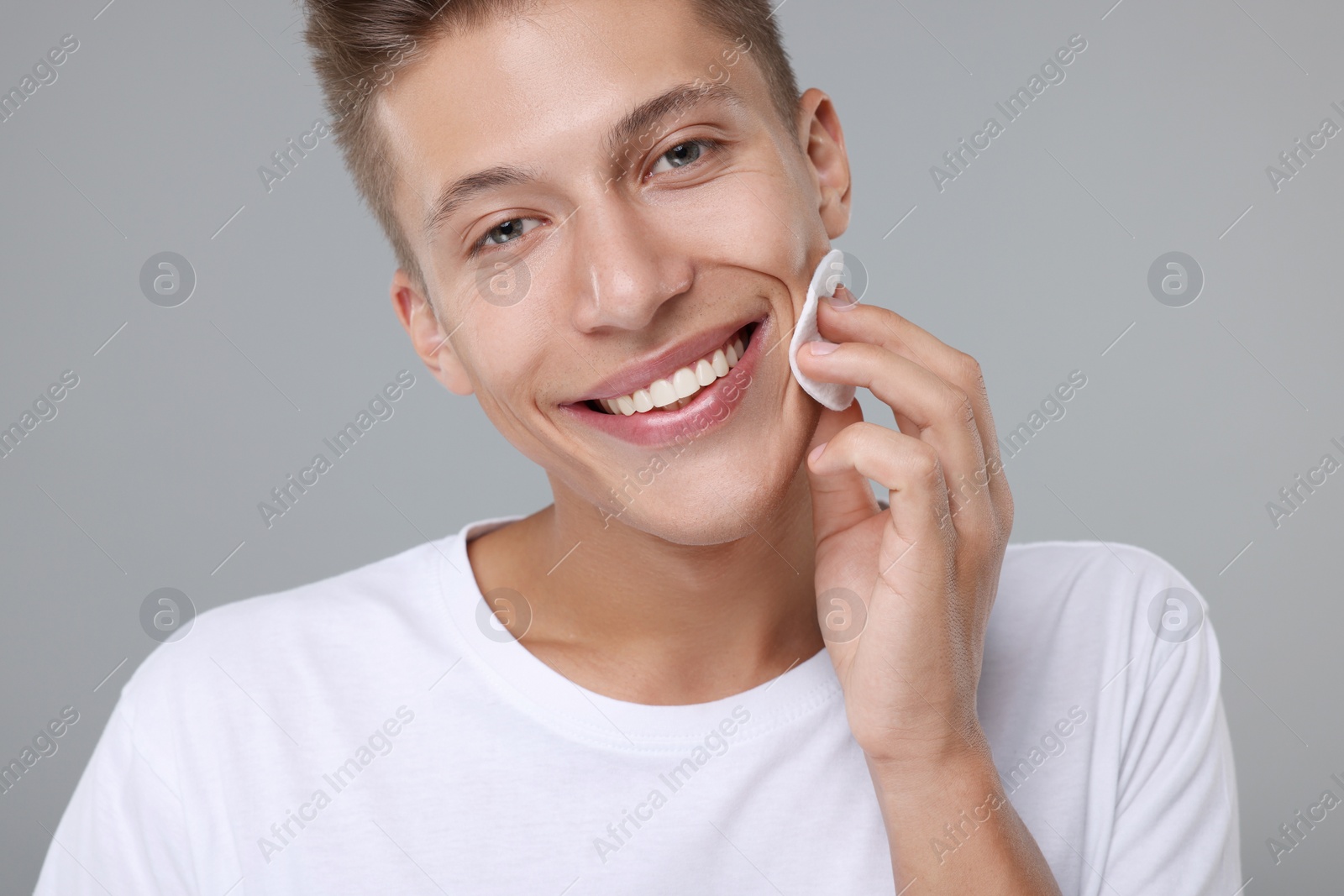 Photo of Handsome man cleaning face with cotton pad on grey background