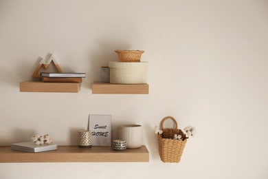 Photo of Wooden shelves with books and different decorative elements on light wall. Space for text