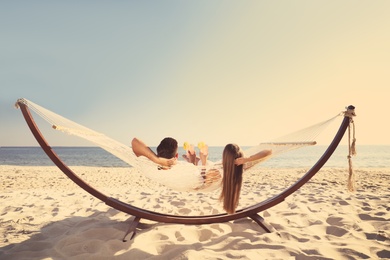 Photo of Couple with refreshing cocktails relaxing in hammock on beach