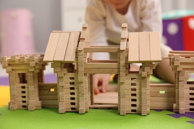 Photo of Little boy playing with wooden entry gate on puzzle mat in room, closeup. Child's toy