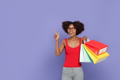 Happy African American woman in glasses with shopping bags on purple background. Space for text