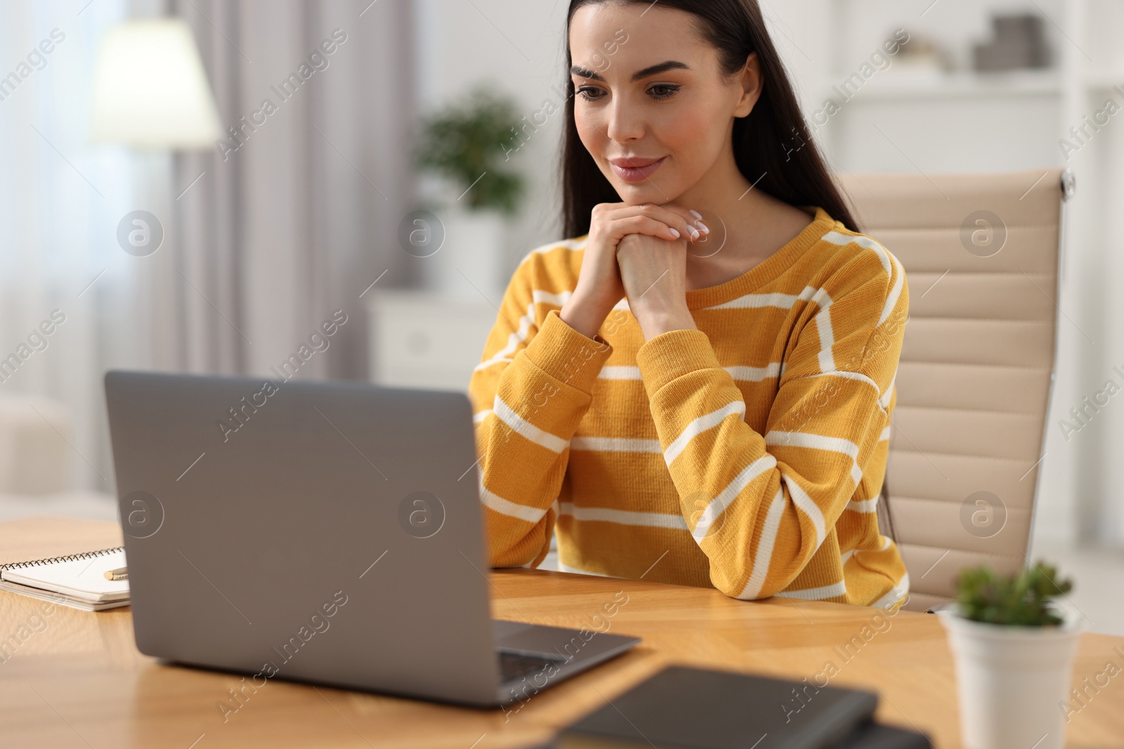 Photo of Young woman watching webinar at table in room