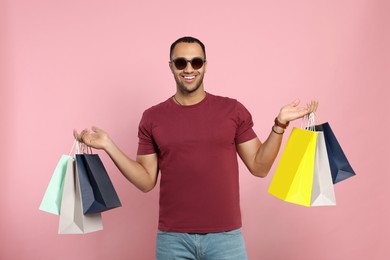 Photo of Happy African American man in sunglasses with shopping bags on pink background