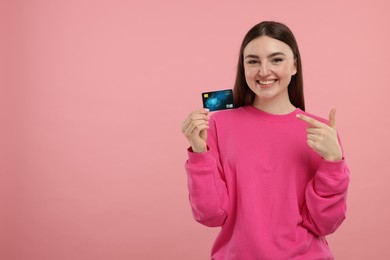 Photo of Happy woman pointing at credit card on pink background, space for text