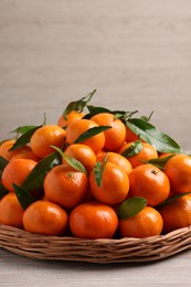 Photo of Fresh ripe juicy tangerines and green leaves on white wooden table