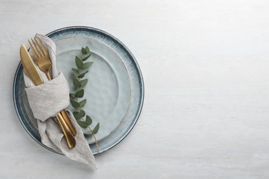 Photo of Stylish setting with cutlery, napkin, eucalyptus branch and plates on white table, top view. Space for text