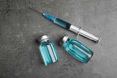 Photo of Vials and syringe with medication on grey table, flat lay. Vaccination and immunization