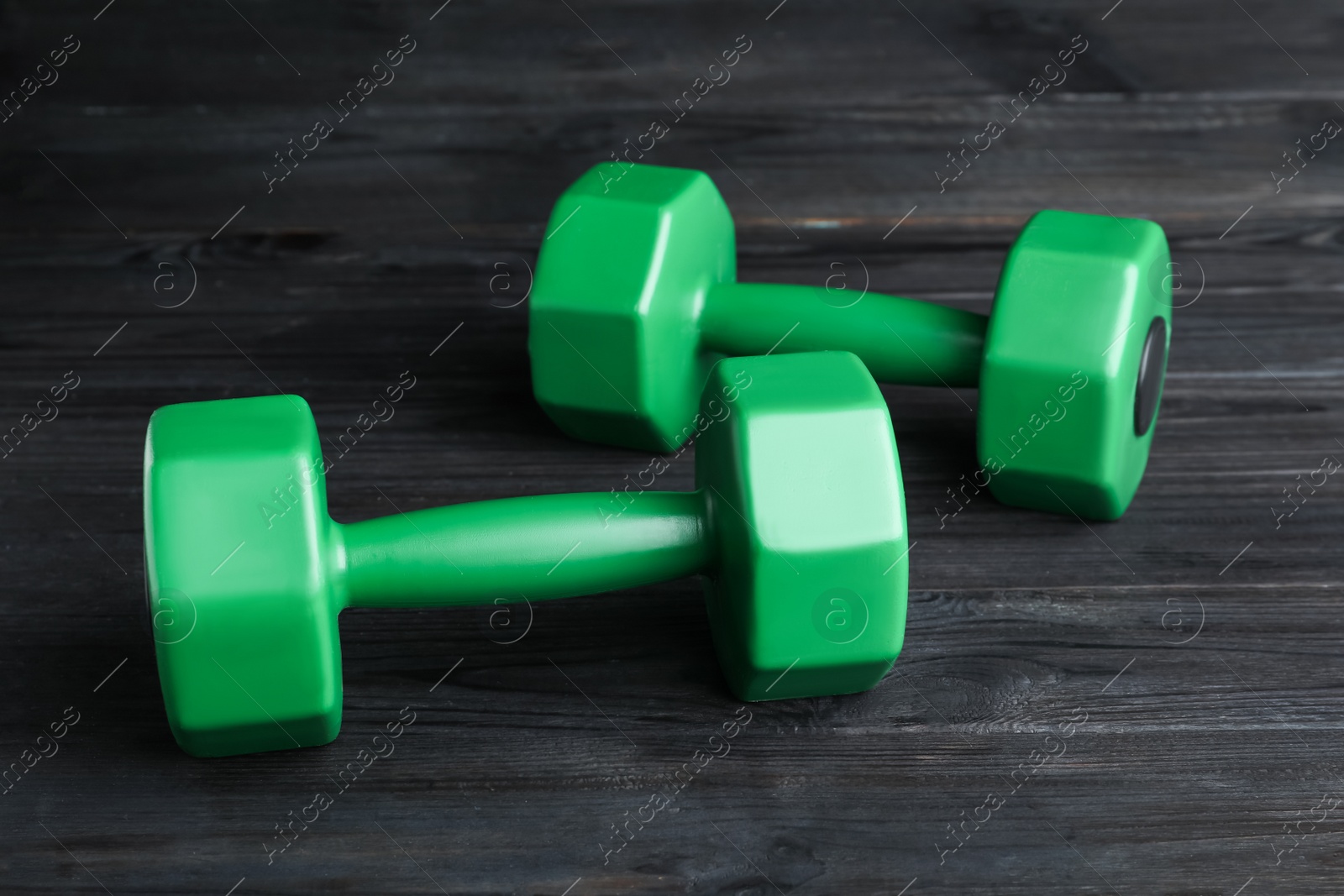 Photo of Green vinyl dumbbells on black wooden table