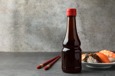 Photo of Bottle of tasty soy sauce, chopsticks and different types of sushi on grey table, space for text