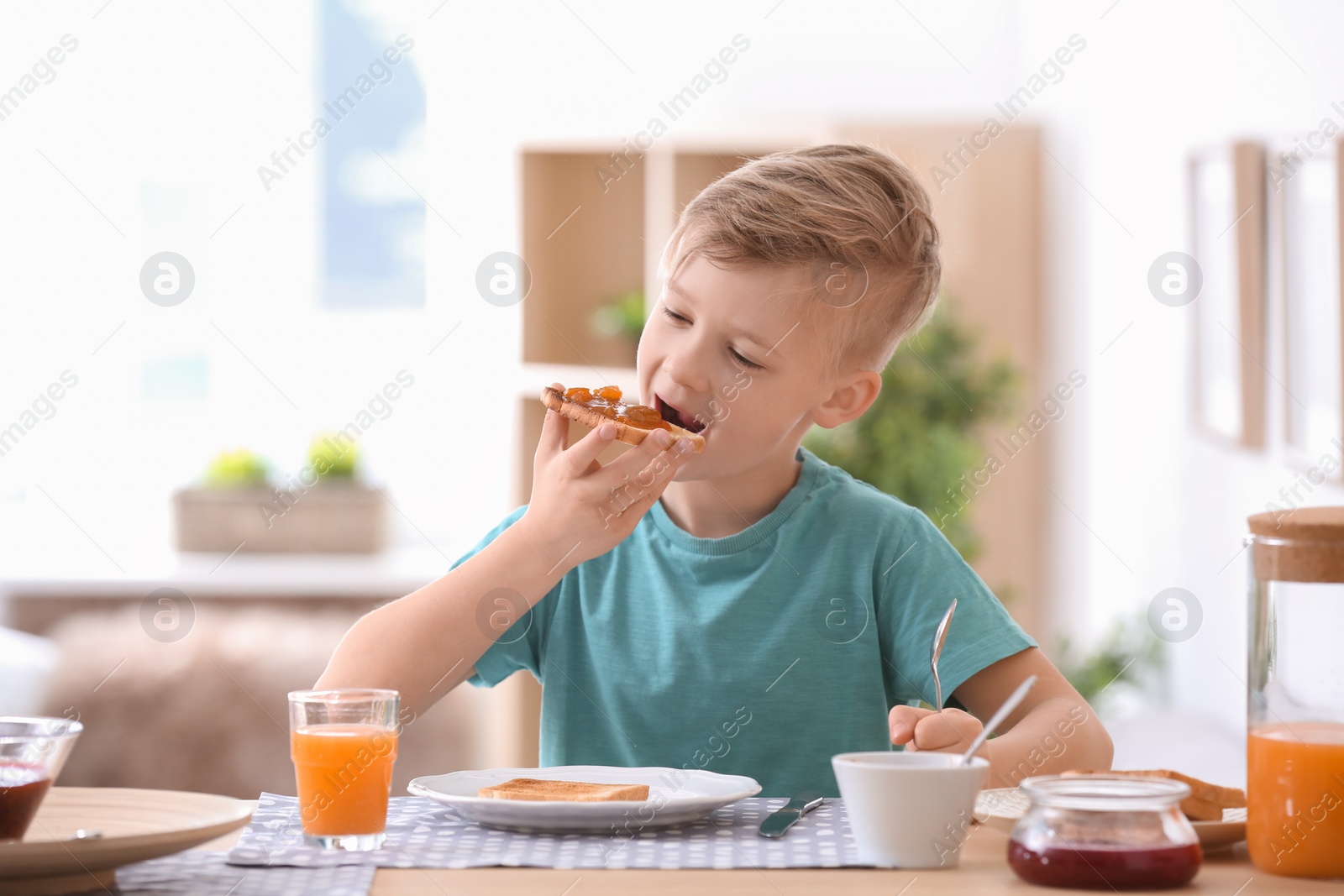 Photo of Cute little boy eating tasty toasted bread with jam at table