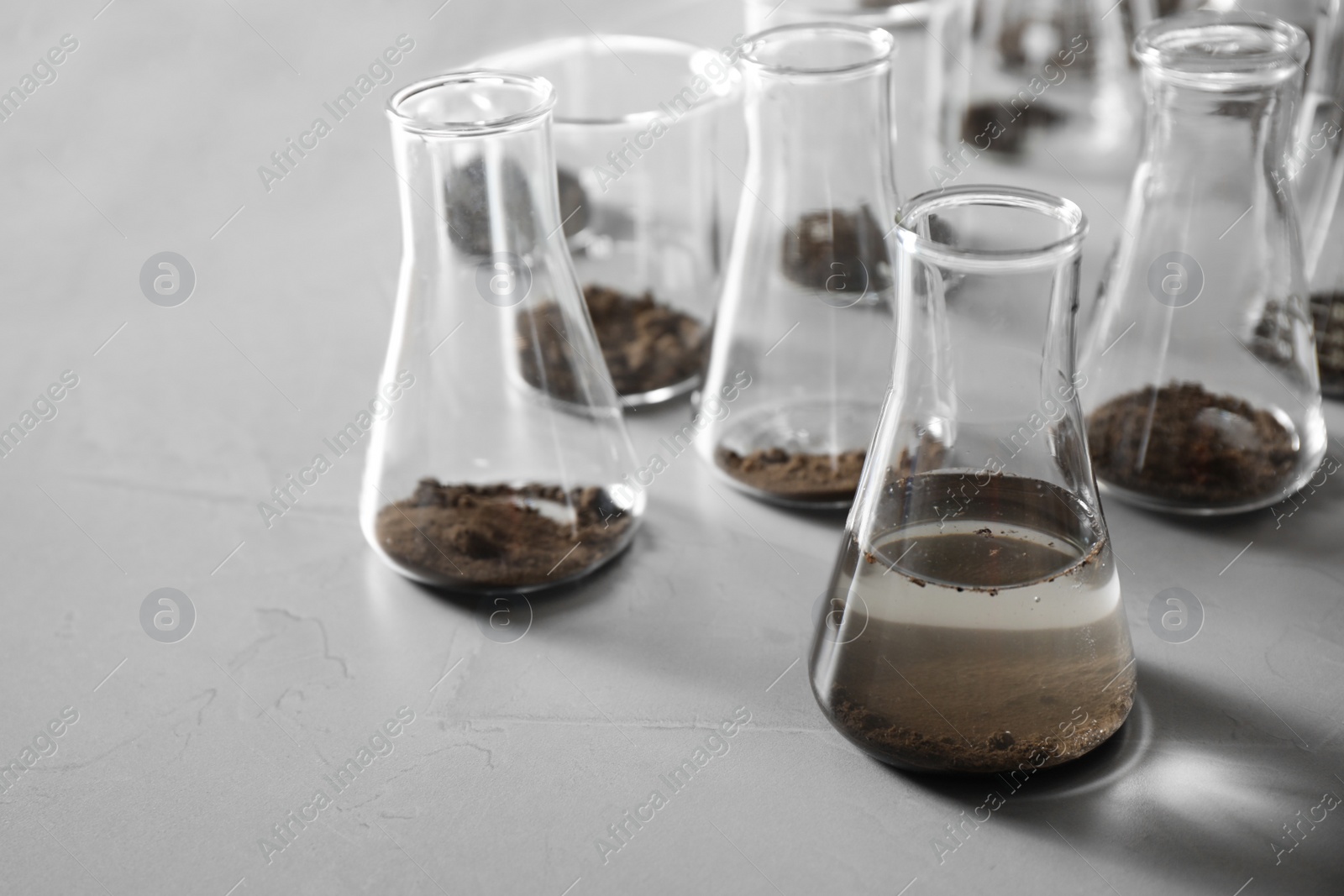 Photo of Glassware with soil samples and extract on grey table. Laboratory research