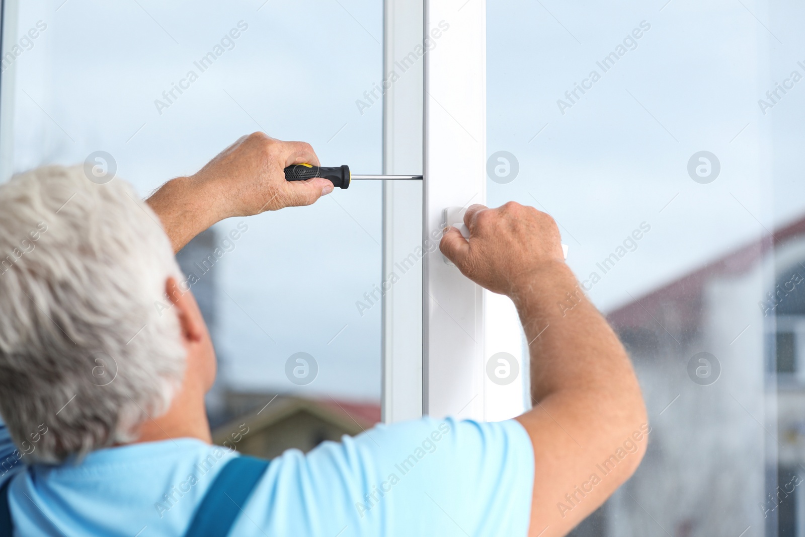 Photo of Mature construction worker repairing plastic window with screwdriver indoors