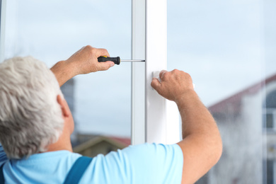 Mature construction worker repairing plastic window with screwdriver indoors