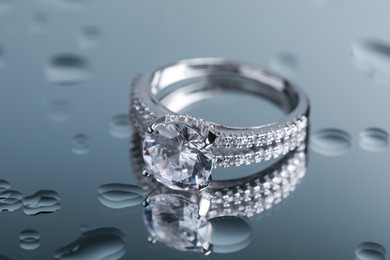 Photo of Luxury jewelry. Stylish presentation of elegant ring on mirror with water drops, closeup
