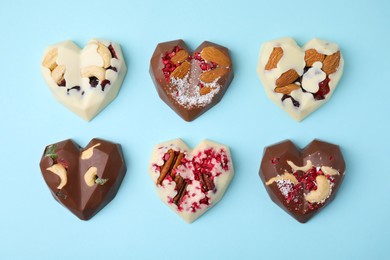 Photo of Tasty chocolate heart shaped candies with nuts on light blue background, flat lay
