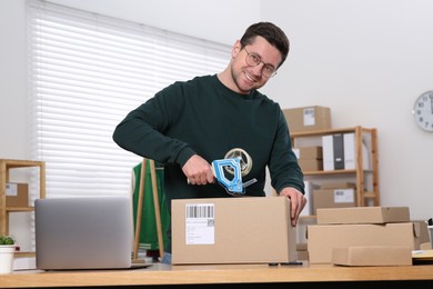 Photo of Seller taping parcel at workplace in office. Online store