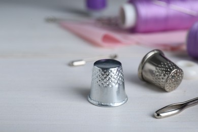 Silver thimbles near sewing tools on white wooden table, closeup. Space for text