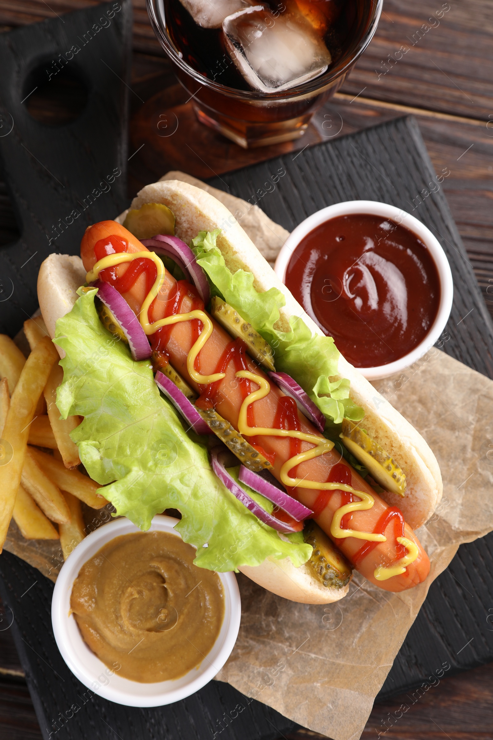 Photo of Delicious hot dog with lettuce, onion and pickle served on wooden table, top view