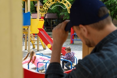 Photo of Suspicious adult man spying on kids at playground, space for text. Child in danger