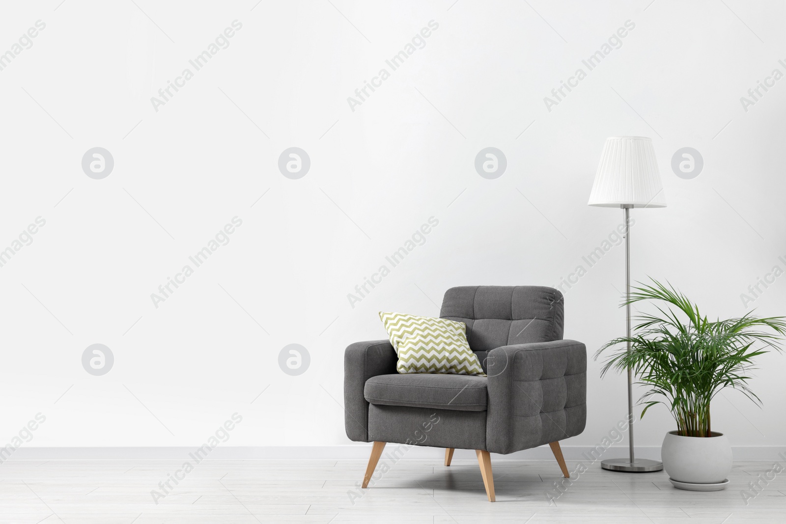 Photo of Stylish living room interior with comfortable armchair, houseplant and lamp near white wall indoors. Space for text