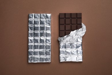 Photo of Tasty chocolate bars wrapped in foil on brown background, flat lay