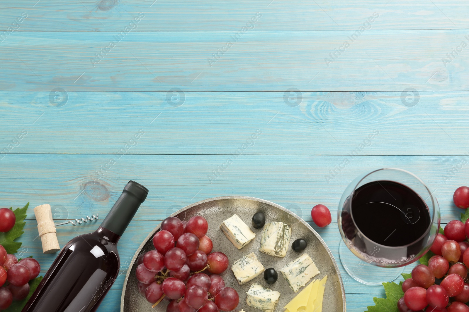 Photo of Tasty red wine and snacks on light blue wooden table, flat lay. Space for text