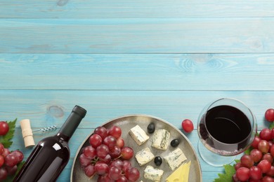 Tasty red wine and snacks on light blue wooden table, flat lay. Space for text