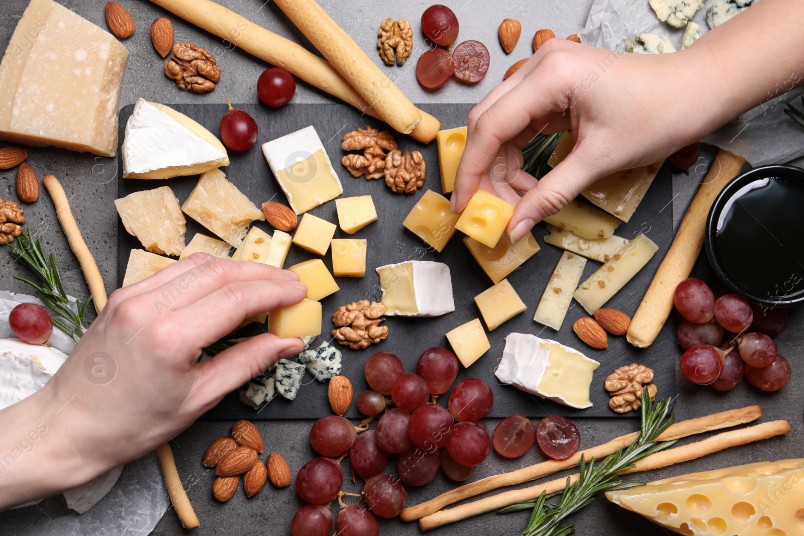 Photo of Women taking pieces from cheese plate on dark table, top view