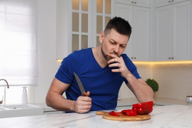 Photo of Man cut finger with knife while cooking at white marble table in kitchen