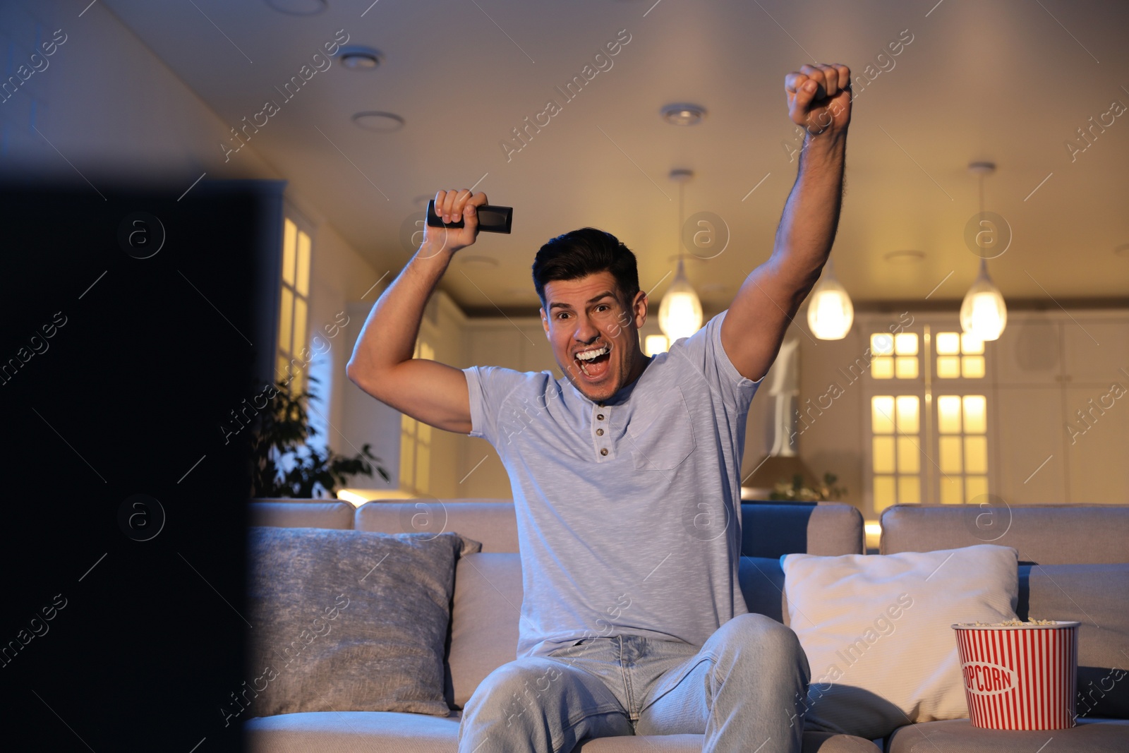 Photo of Man watching movie with popcorn on sofa at night