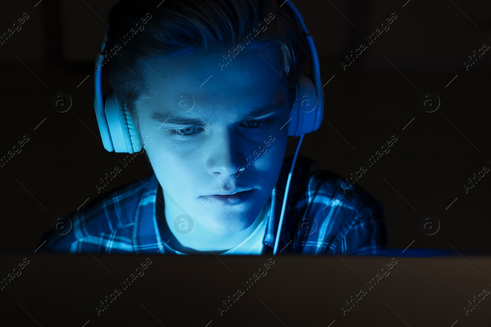 Photo of Teenage boy in headphones using computer at night. Internet addiction