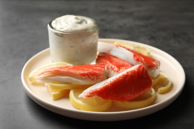 Delicious crab sticks with lemon slices and sauce on grey table