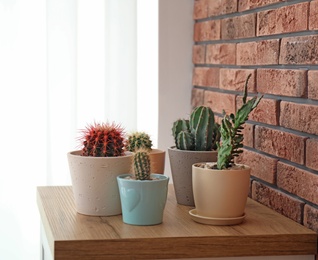 Photo of Beautiful cacti in flowerpots on table near brick wall