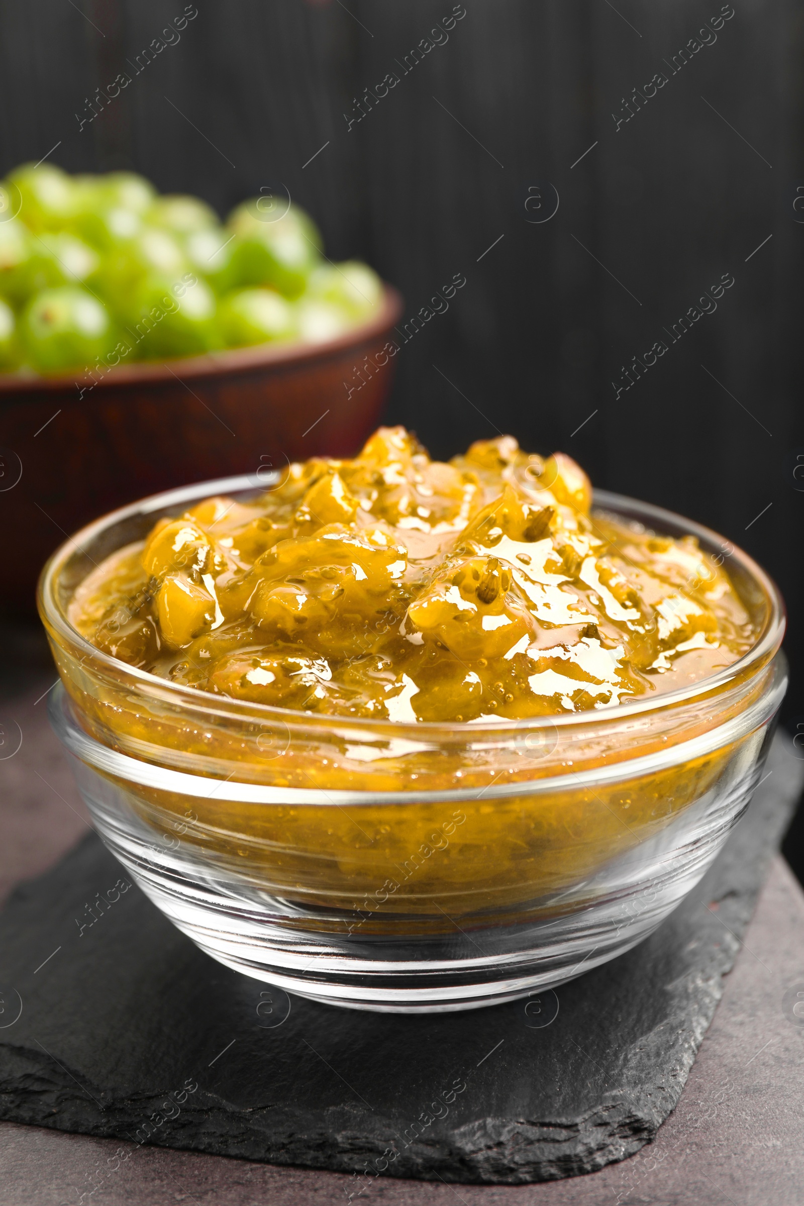 Photo of Delicious gooseberry jam in glass bowl on grey table, closeup