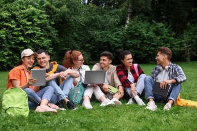 Group of happy young students learning together on green grass in park