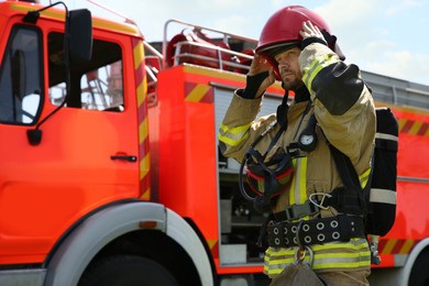 Photo of Firefighter in uniform wearing helmet near fire truck outdoors