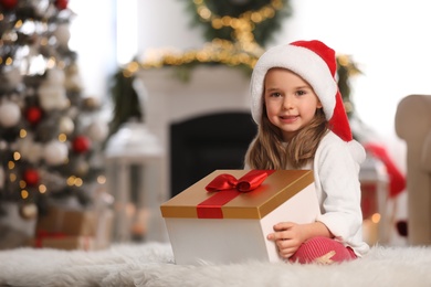 Photo of Cute little girl holding gift box in room decorated for Christmas